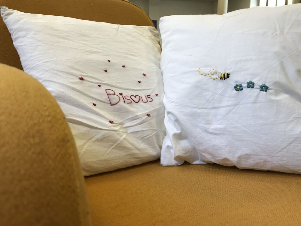 Un coussin avec le texte bisous et de petits coeurs et un autre avec une abeille et des fleurs